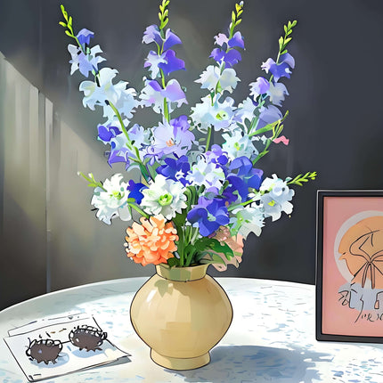 Handmade delphinium artificial flower arrangement in a vase on a table with decorative items.