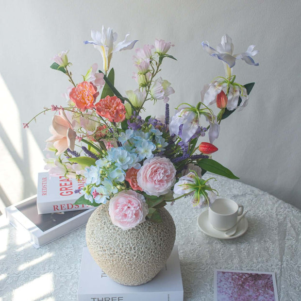 Realistic artificial Peony flower arrangement in decorative vase on table with books and tea set.