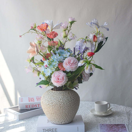 Realistic artificial Peony flower arrangement in a decorative vase on a table with books and a coffee cup.