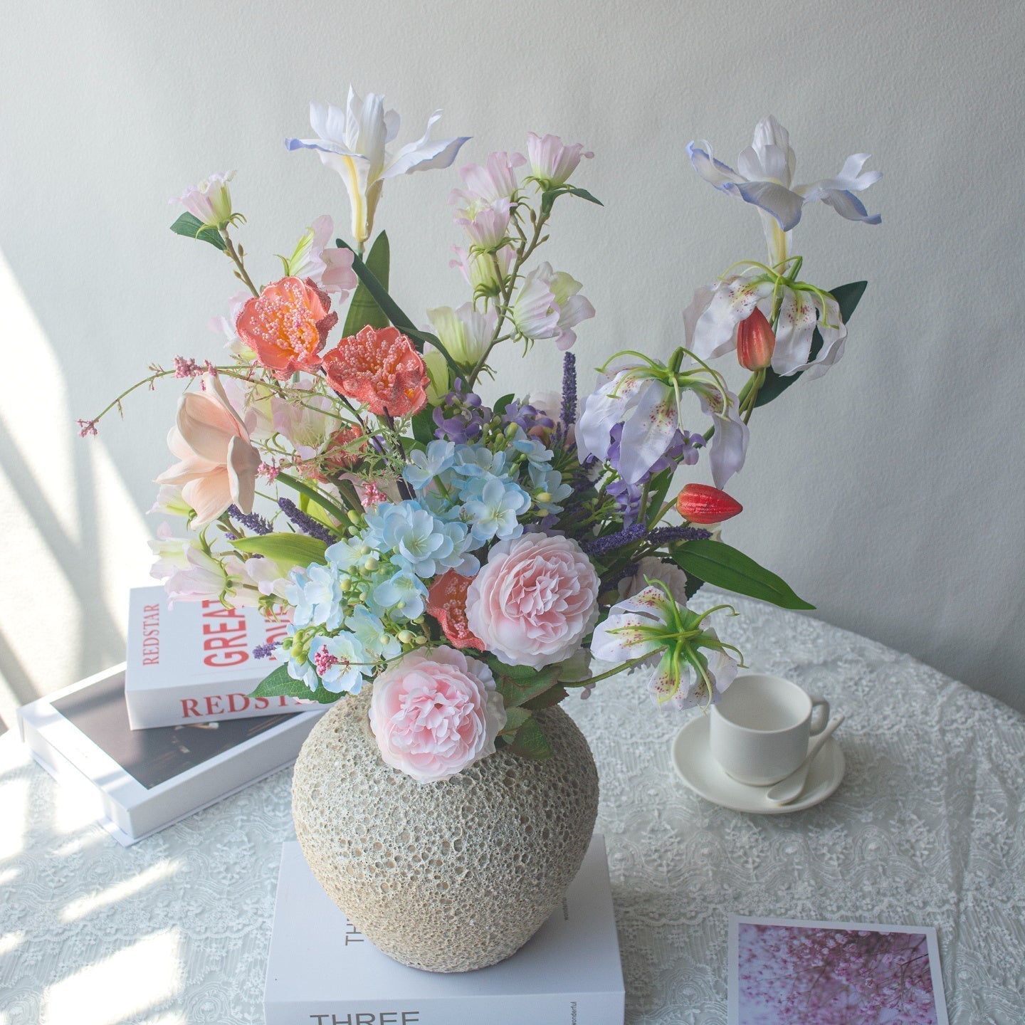 Artificial Flower Bouquets arrangement in a decorative vase on a table with books and a coffee cup.