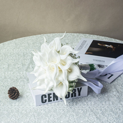 Handmade lifelike artificial white calla lily bouquet displayed on a table with books and a pinecone.